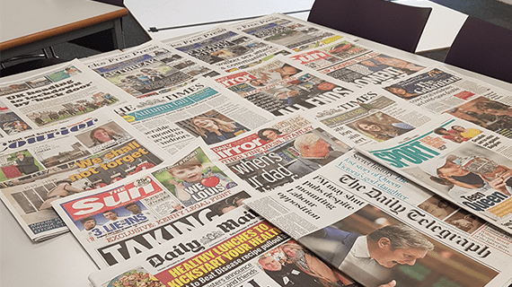 Newspapers all laid out on a table overlapping one another