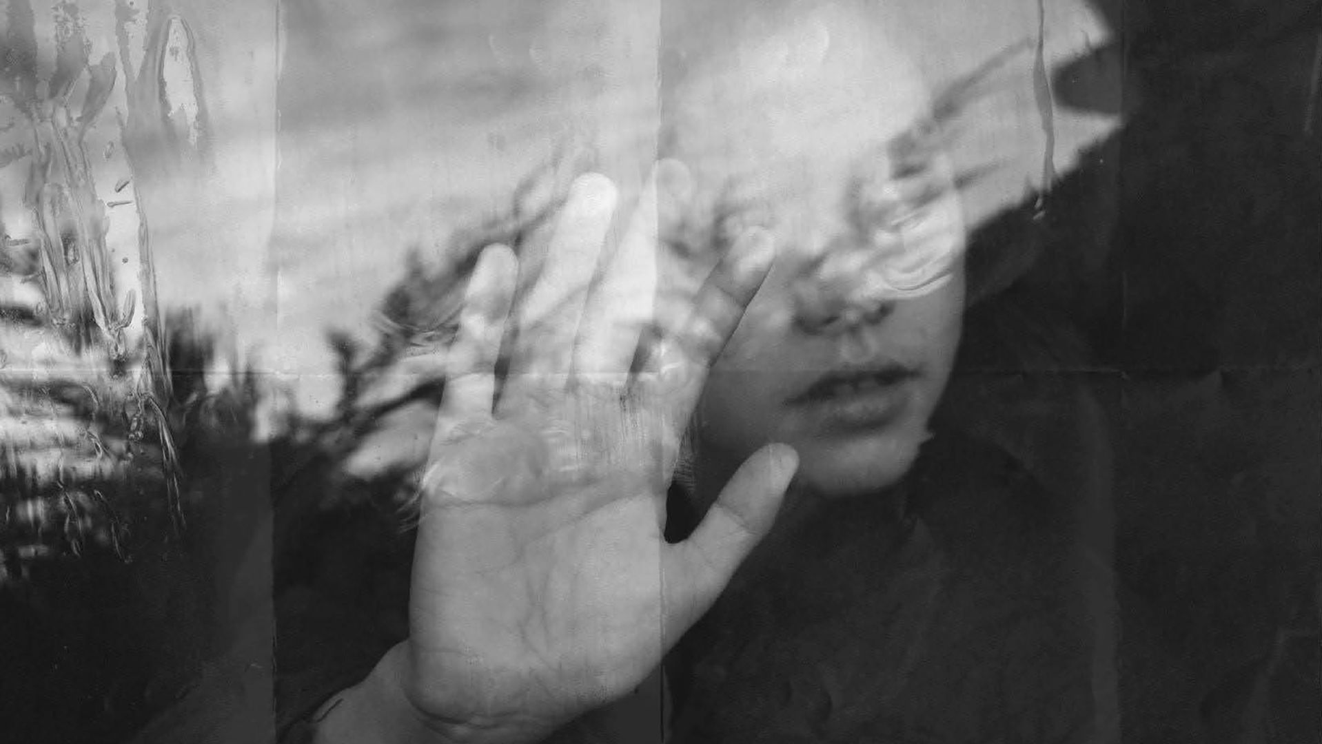 A girl pressing her hand against a window whilst staring out into the distance