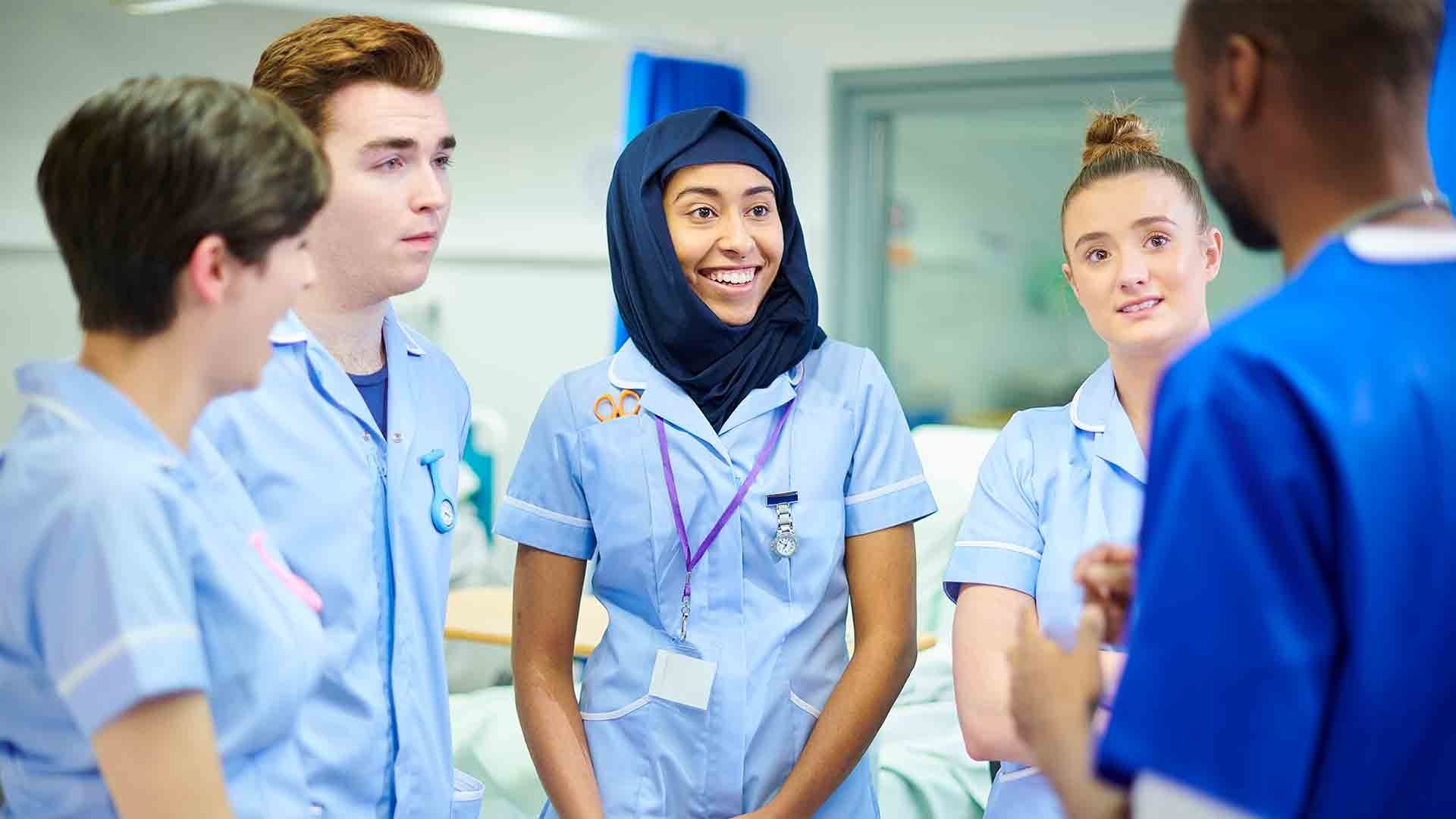 A group of five student nurses stood in a circle looking at one another smiling