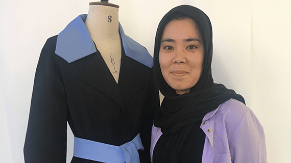 A BNU Fashion and Textiles student stood next to her garment smiling towards the camera