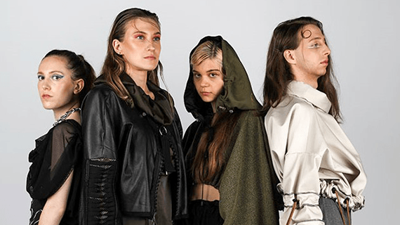 Four Fashion Design students stood posing back to back for a photoshoot against a grey wall