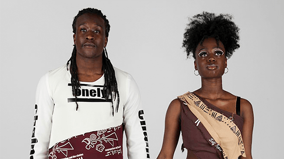 Two Fashion Design students stood side by side holding hands modelling their clothes