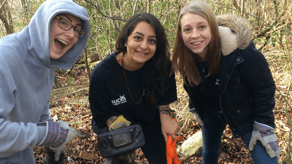 Three BNU students stood posing for a photo in the woods whilst holding a metal detector