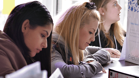 Three BNU students sat at a table sat next to one another taking notes on paper