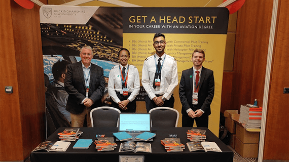 Four BNU Aviation staff/students in uniform stood behind a table with a range of flyers on