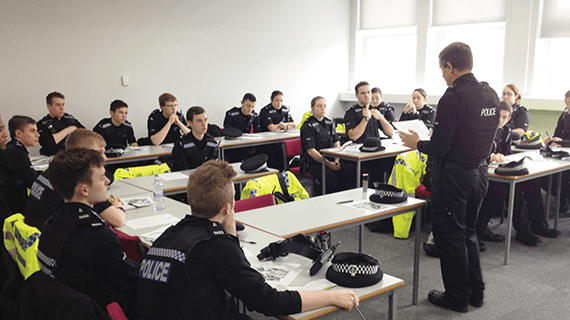 Policing students sat in a classroom listening to a teacher who is stood facing the students