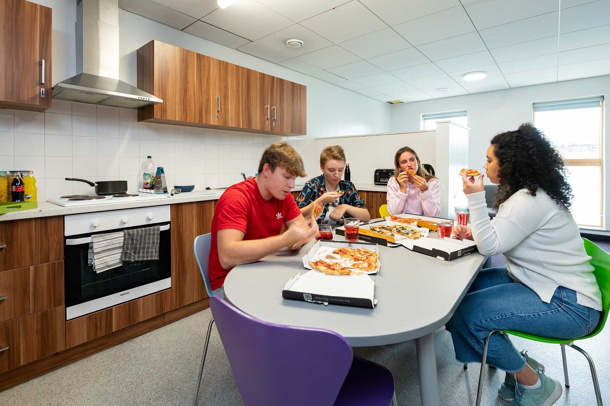 four students eating pizza at a kitchen table in Windsor House accommodation