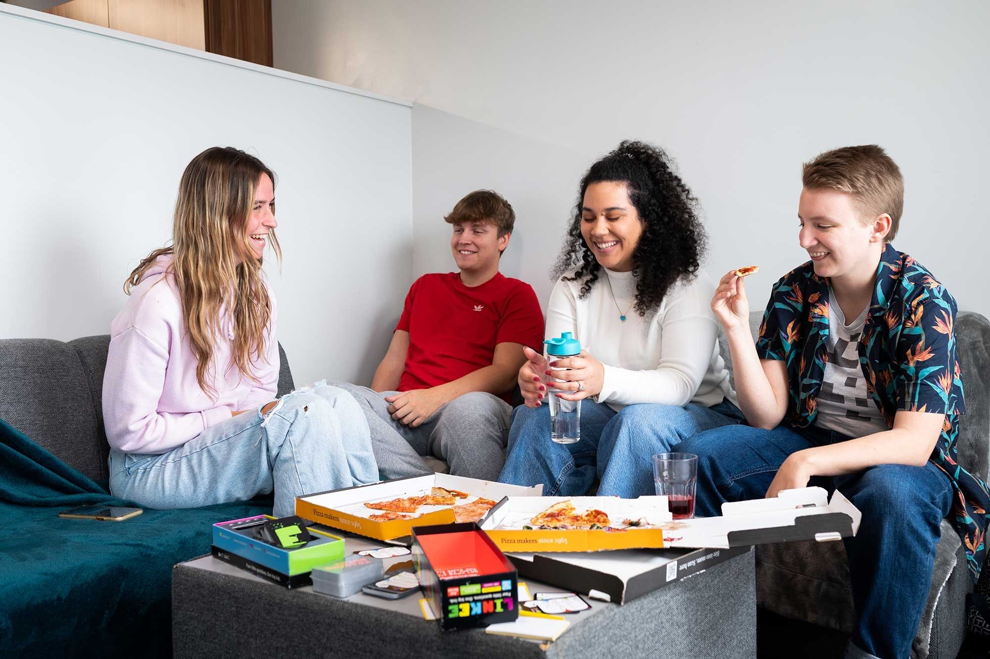 Four students eating pizza in a lounge area in Windsor House accommodation