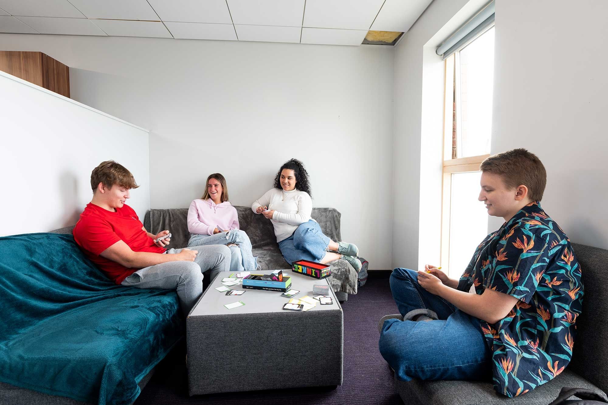 Four students playing a board game in a lounge area in Windsor House accommodation