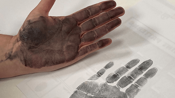 A Criminology student with ink on their hand as they put their hand against a piece of paper