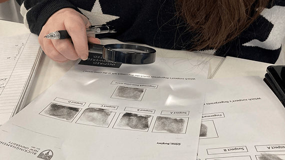 The hand of a student looking at the finger prints left by various people on a piece of paper