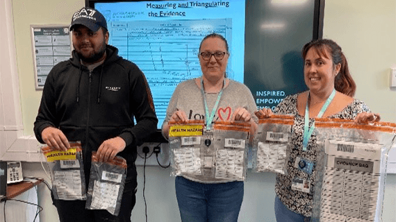 Three Criminology students holding forensic bags and smiling towards the camera