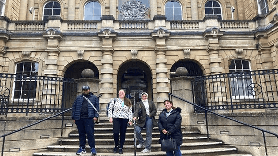 Four Criminology students stood on the stairs outside a building facing towards the camera