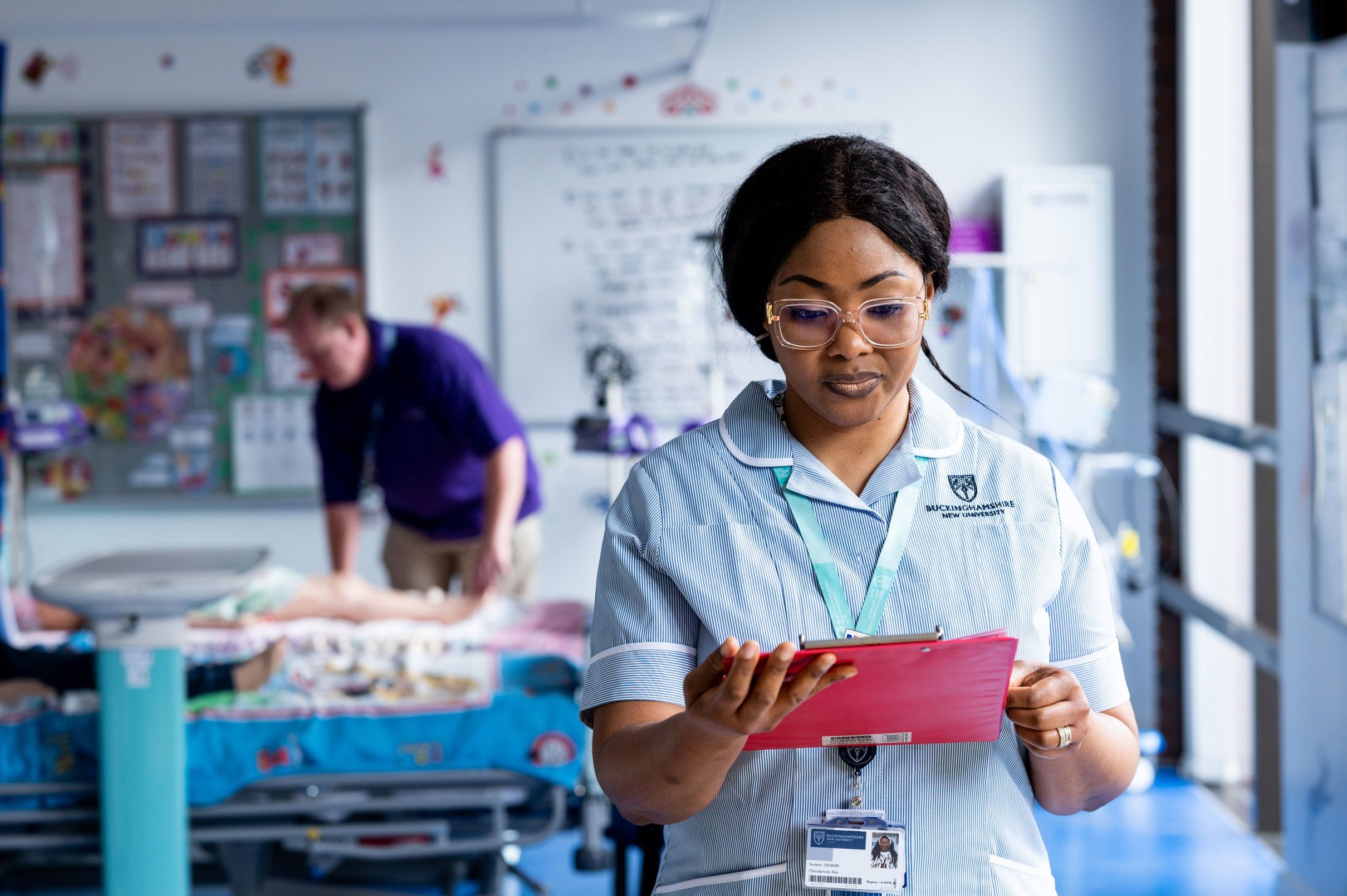 A student nurse in uniform stood in a simulation ward looking down at a tablet screen