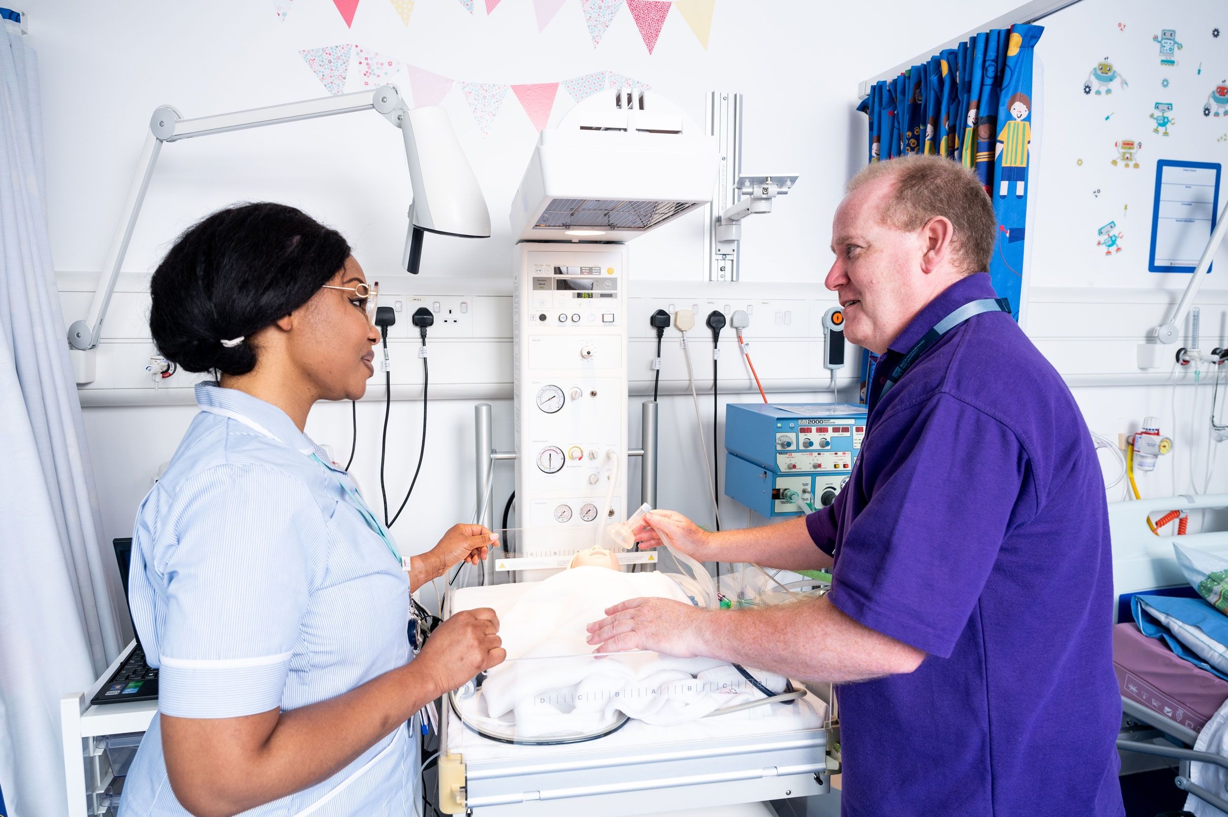 A student nurse stood in a simulation ward next to a lecturer giving words of advice