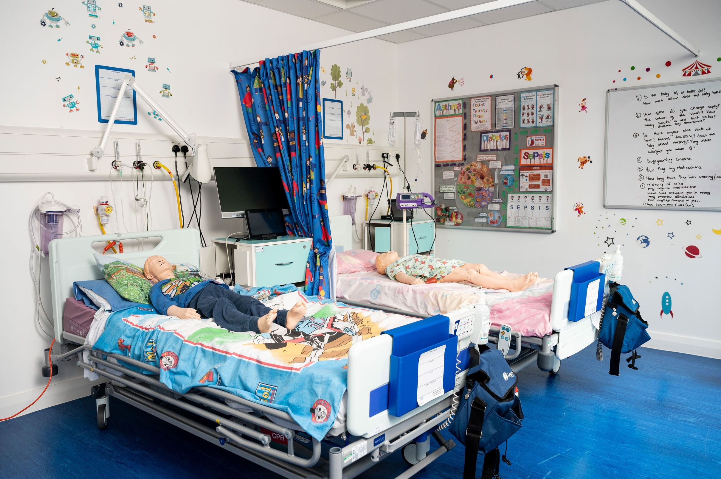 Two hospital beds in a simulation room with dummy children laying on them