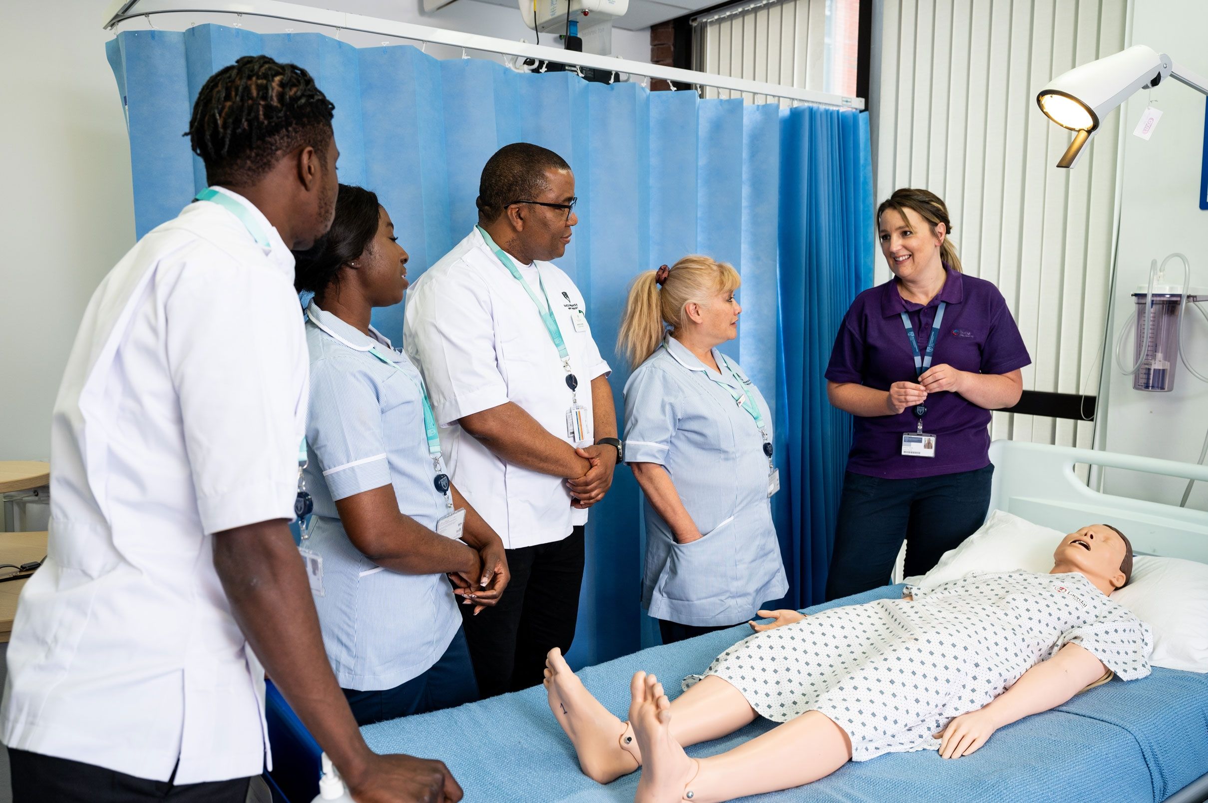 Four nursing students in uniform stood around a simulated hospital bed as a dummy child lays on the bed