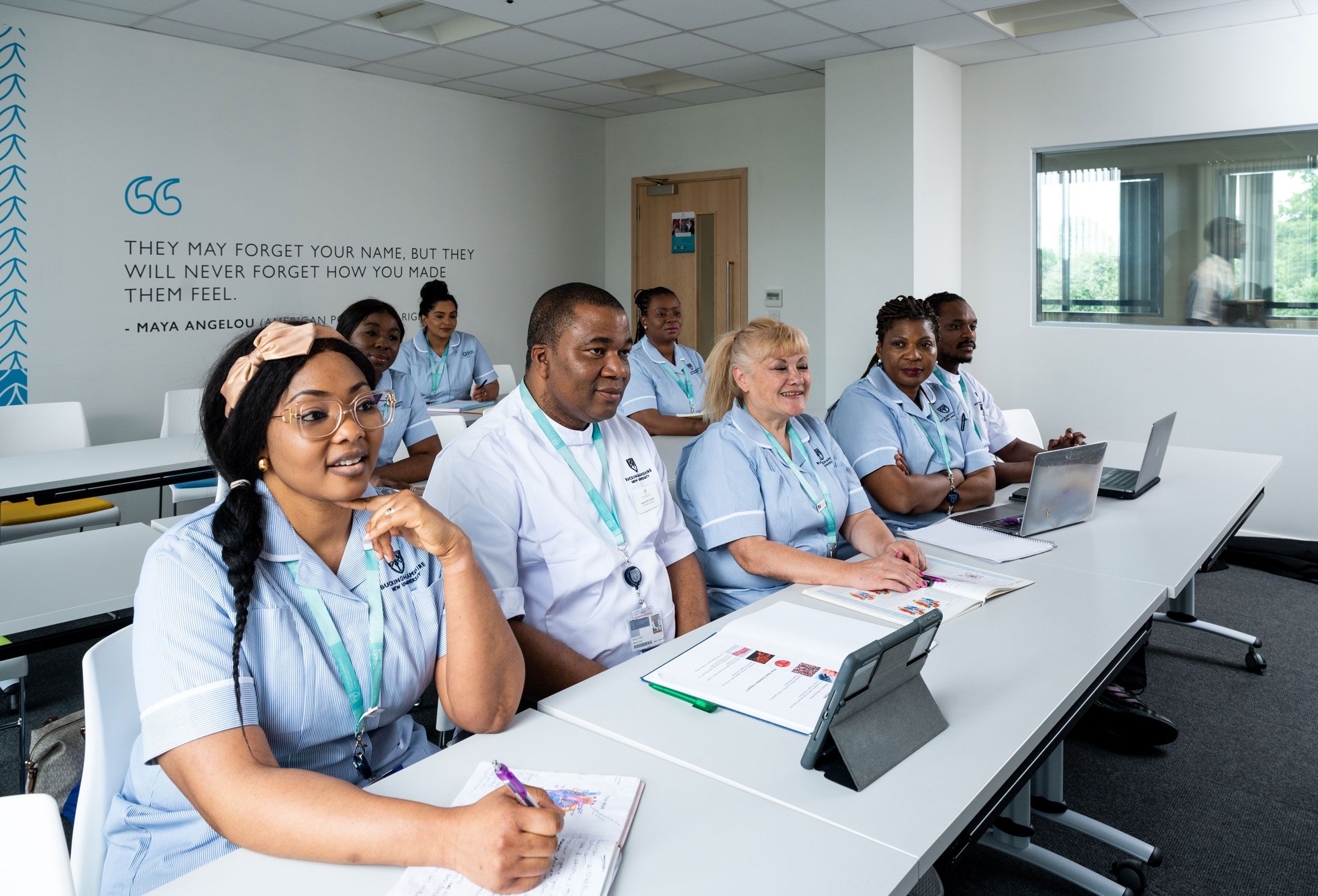 Eight nursing students sat in their uniform in a classroom facing the front of the room with textbooks open