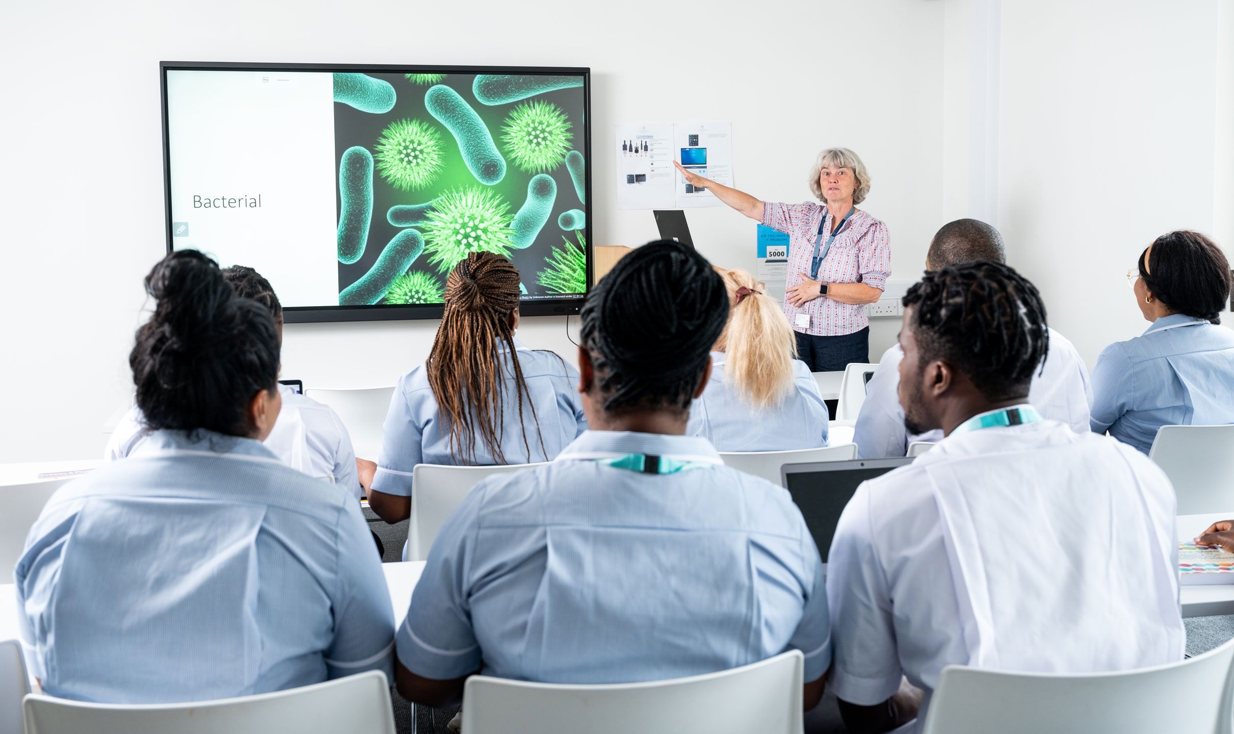 Nursing students facing the front of a classroom as a teacher delivers a class on a whiteboard