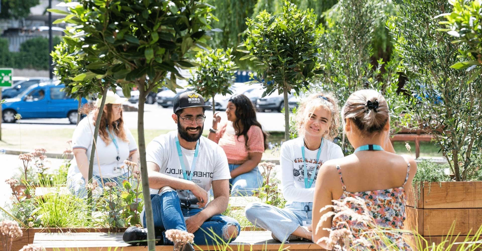 Five BNU students sat on wooden benches in amongst trees on concourse in the sunshine