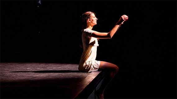 Musical Theatre student sat on a stage in the spotlight