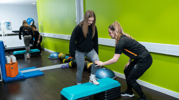 A woman lifting her leg onto a step as she undergoes fitness testing from a member of BNU staff.