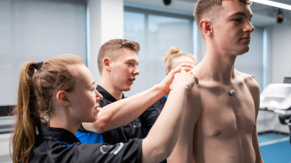 Two Sports Therapy students assessing the shoulders of a fellow student.