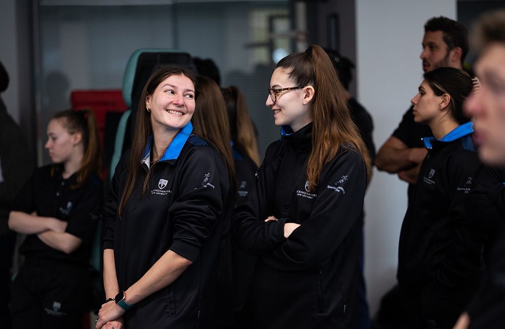 Two Sports Therapy students in uniform looking and smiling at one another
