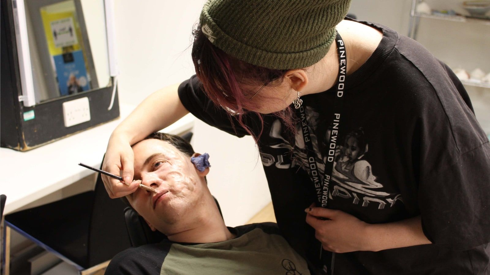A special effects student applies a mask to a student lying down.