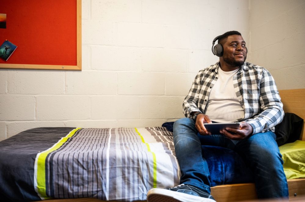 Smiling student sitting on a bed in student accommodation