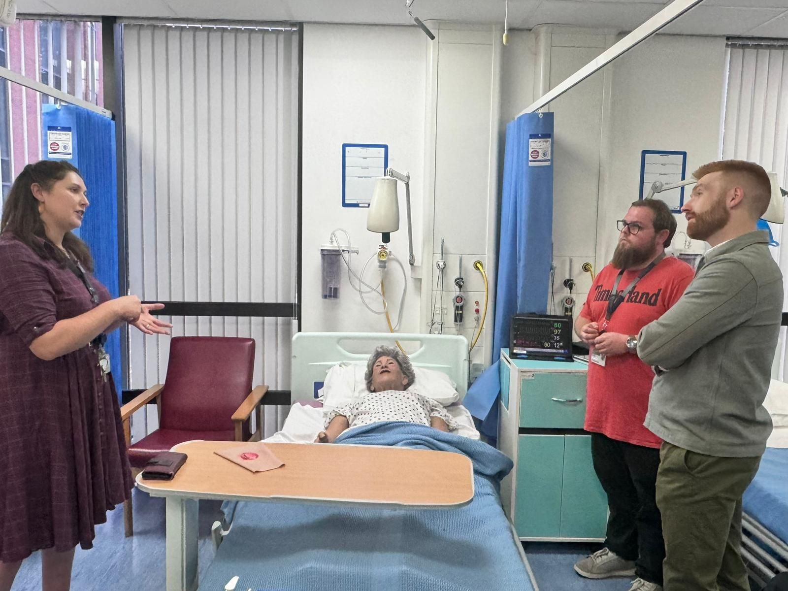 Three people surrounding a dummy patient 