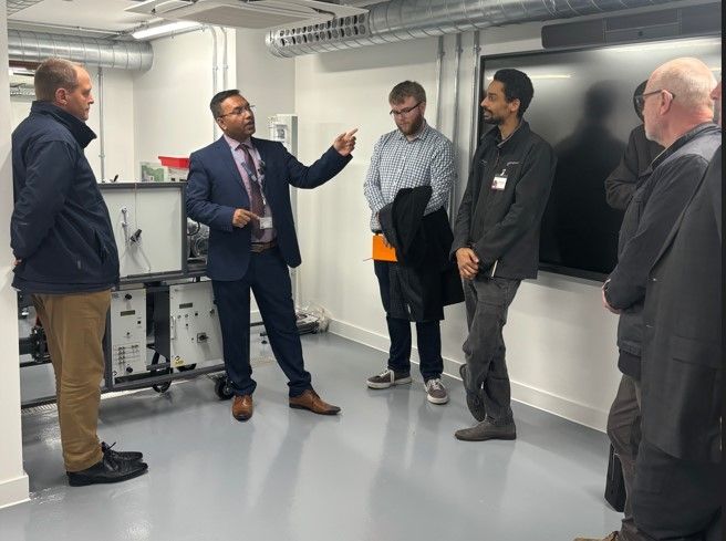 Man in an engineering room with equipment speaking to others 
