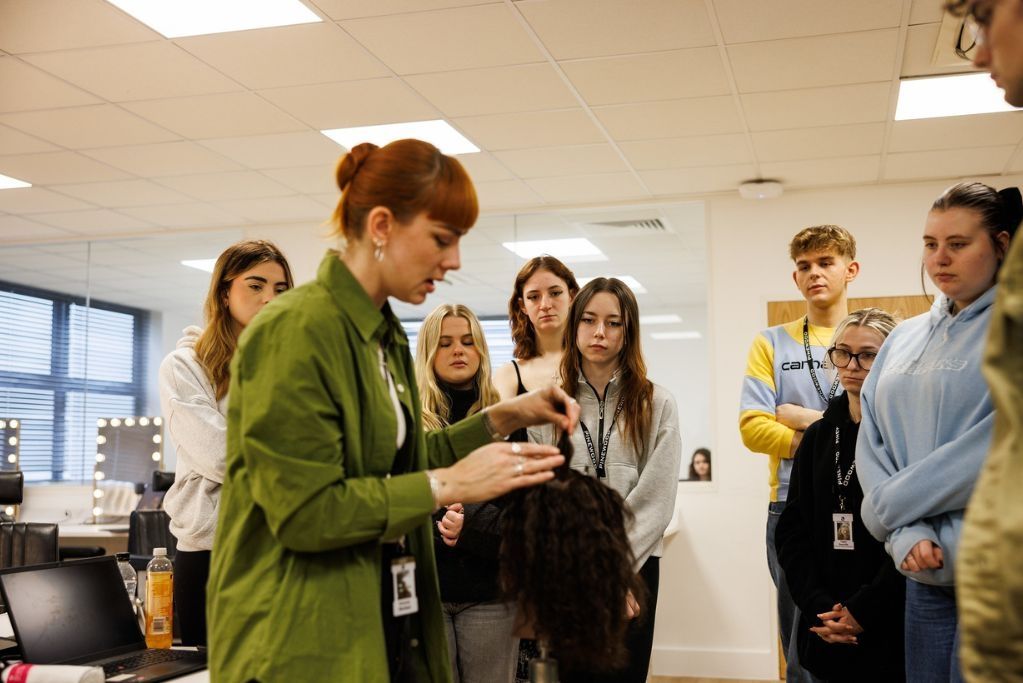 A Hair and Make-up lecturer styling a dummies hair with 8 students stood around watching.