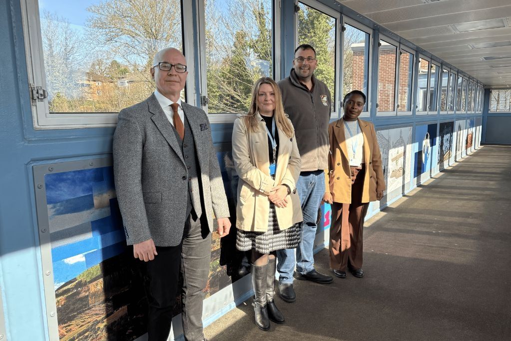Four people stood together on a train station bridge posing for a photo