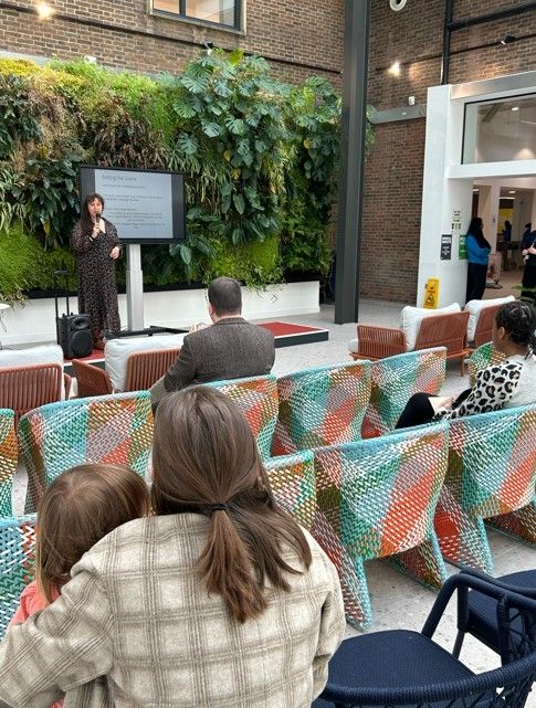 A woman in front of a large group presenting. She is holding a microphone.