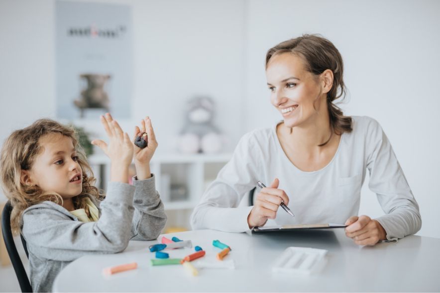 Occupational Therapist supporting a young child sat at a table through play therapy.