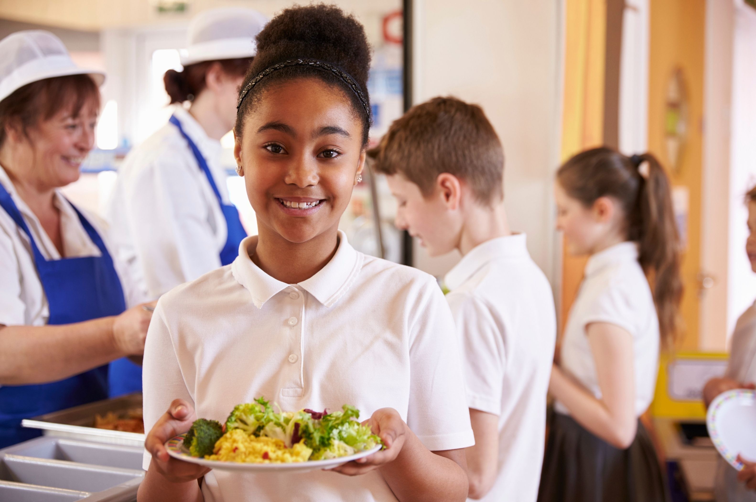 Child holding a plate of food in a school cafeteria