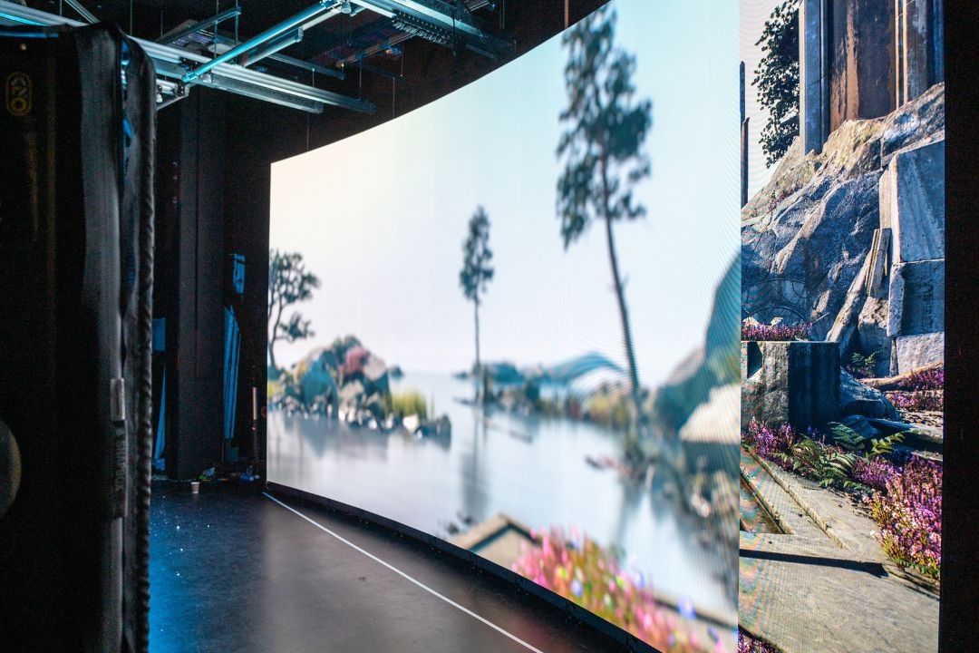 A large LED wall screen with a backdrop of a trees and water on display in a Film and TV studio.