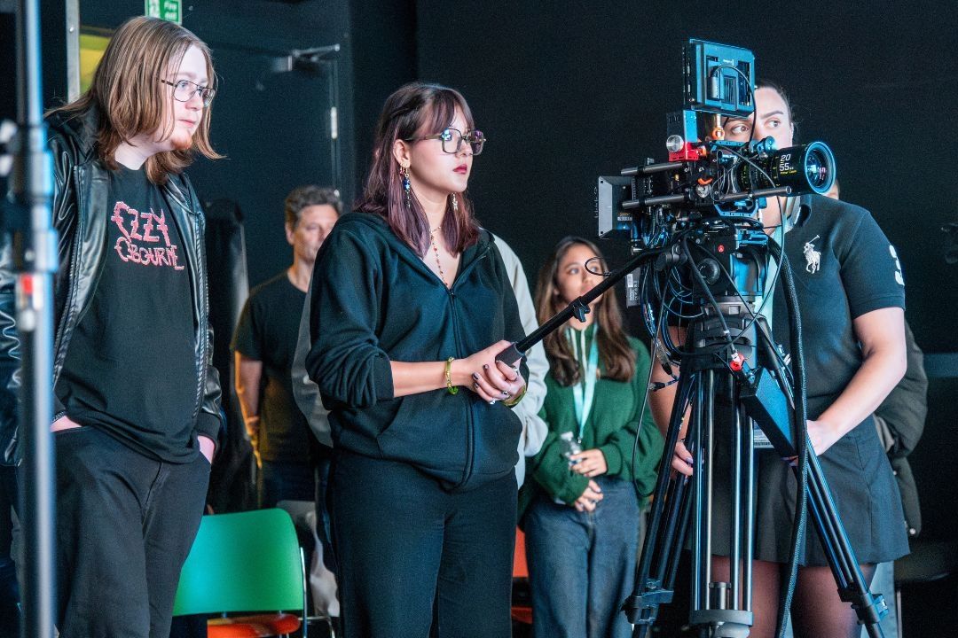 A student operating a camera in the Film and TV Studio, two fellow students stand either side of her.