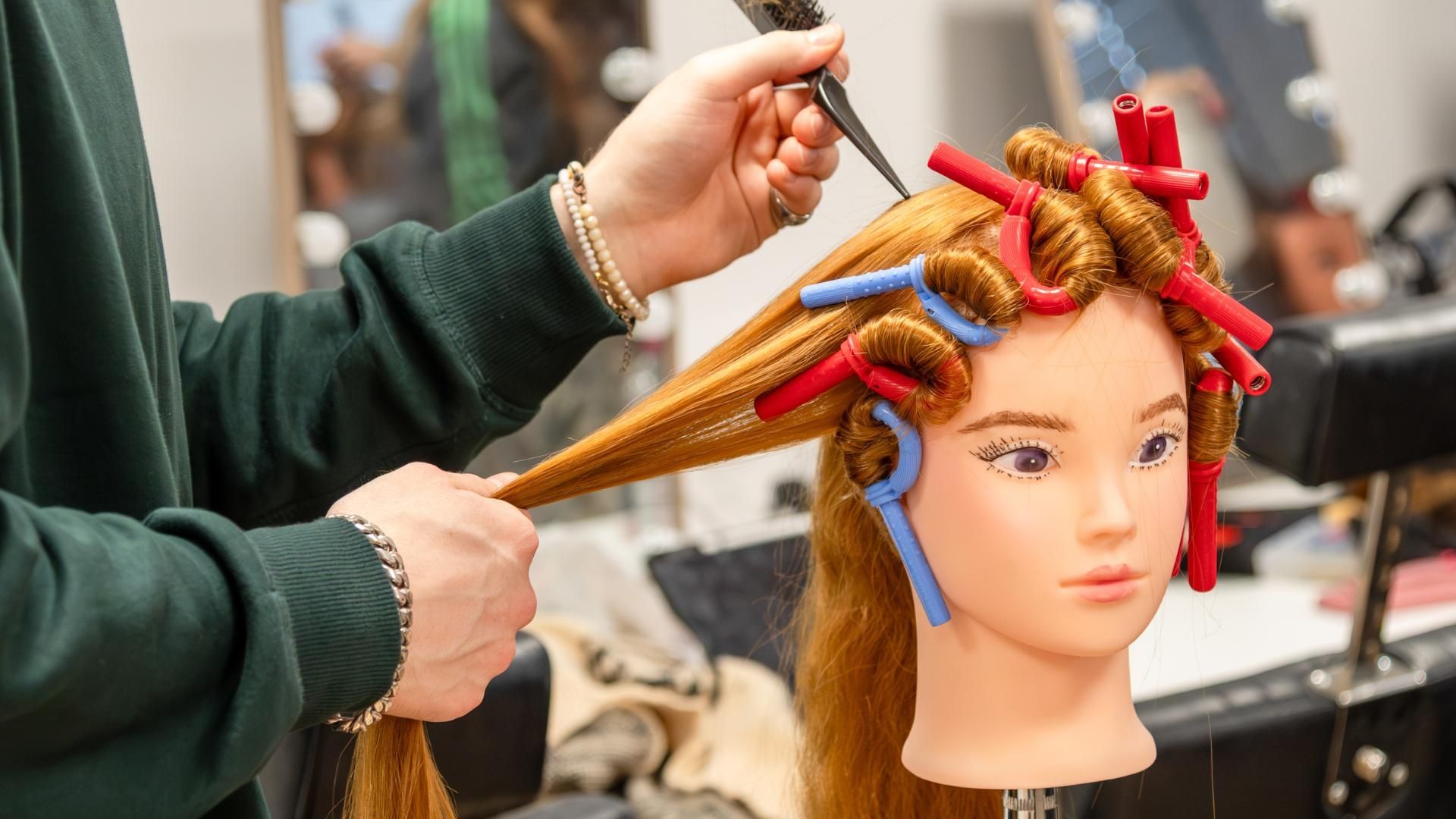 A hair and make-up student working on the hair on a dummy wig.