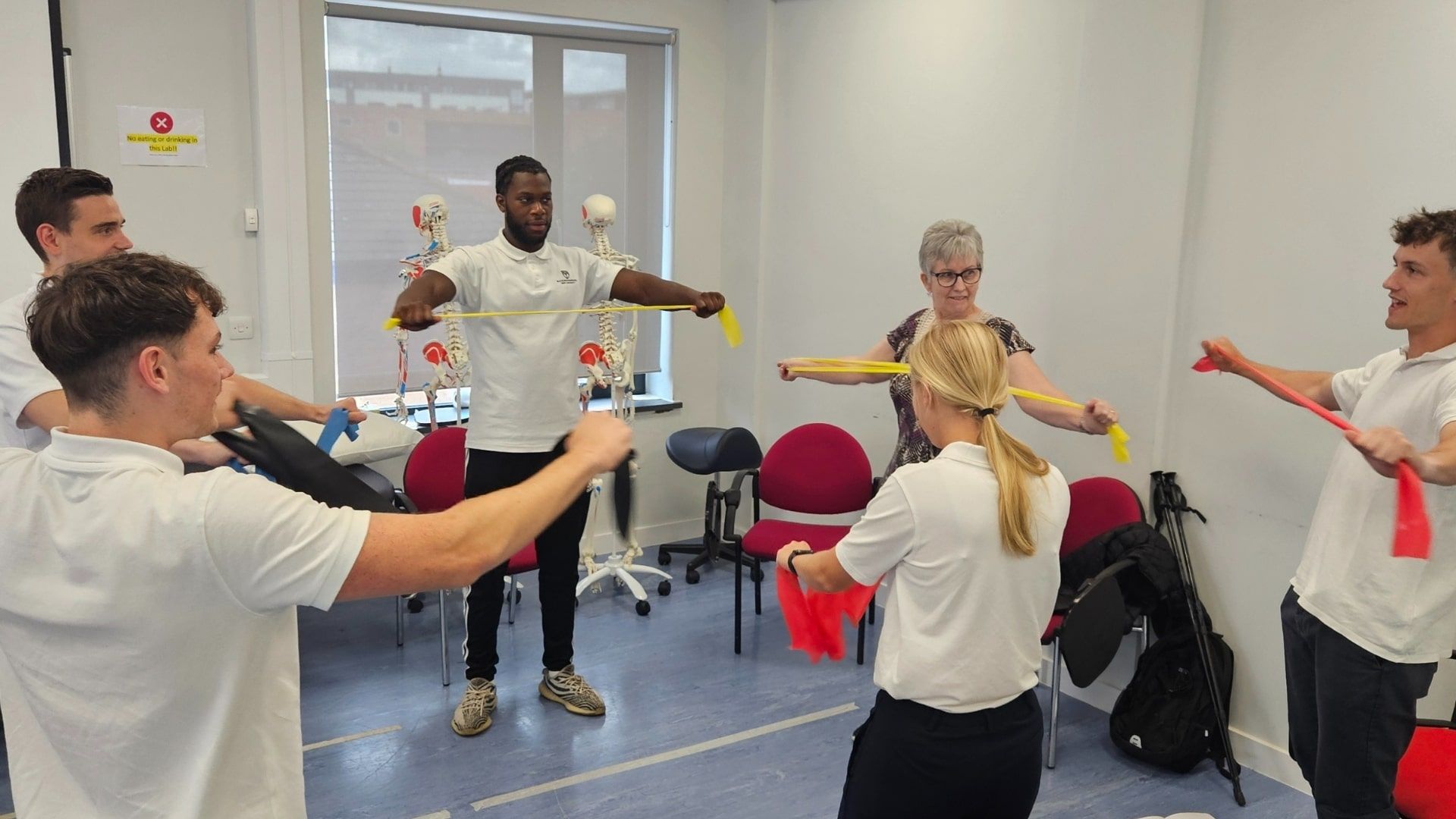 Five Physiotherapy students stood in a cricle pulling on resistance bands alongside a member of the public.