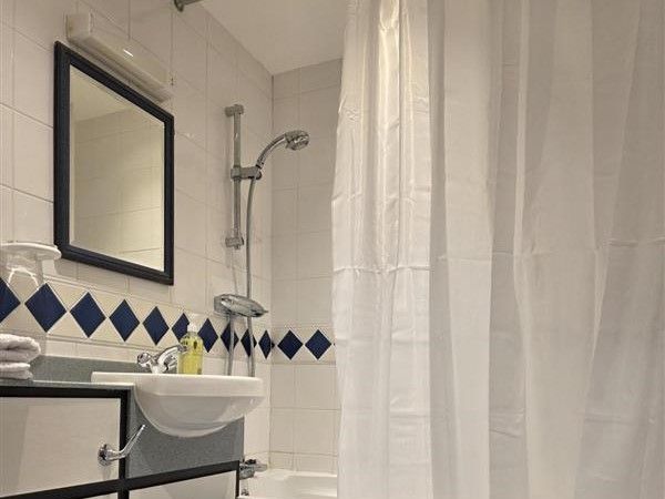Bathroom interior at Alex House showing bathtub with shower head and shower curtain, sink and mirror