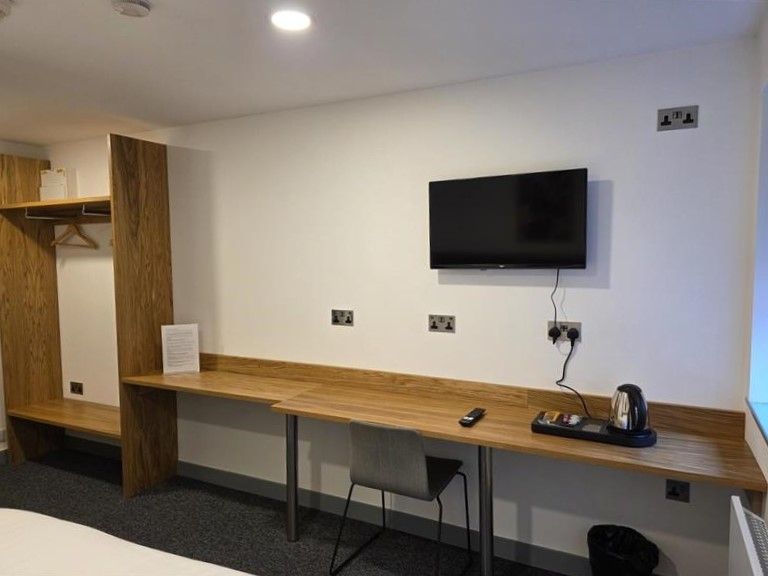 Bedroom interior at Alex House showing desk with chair and kettle, wardrobe and wall-mounted TV