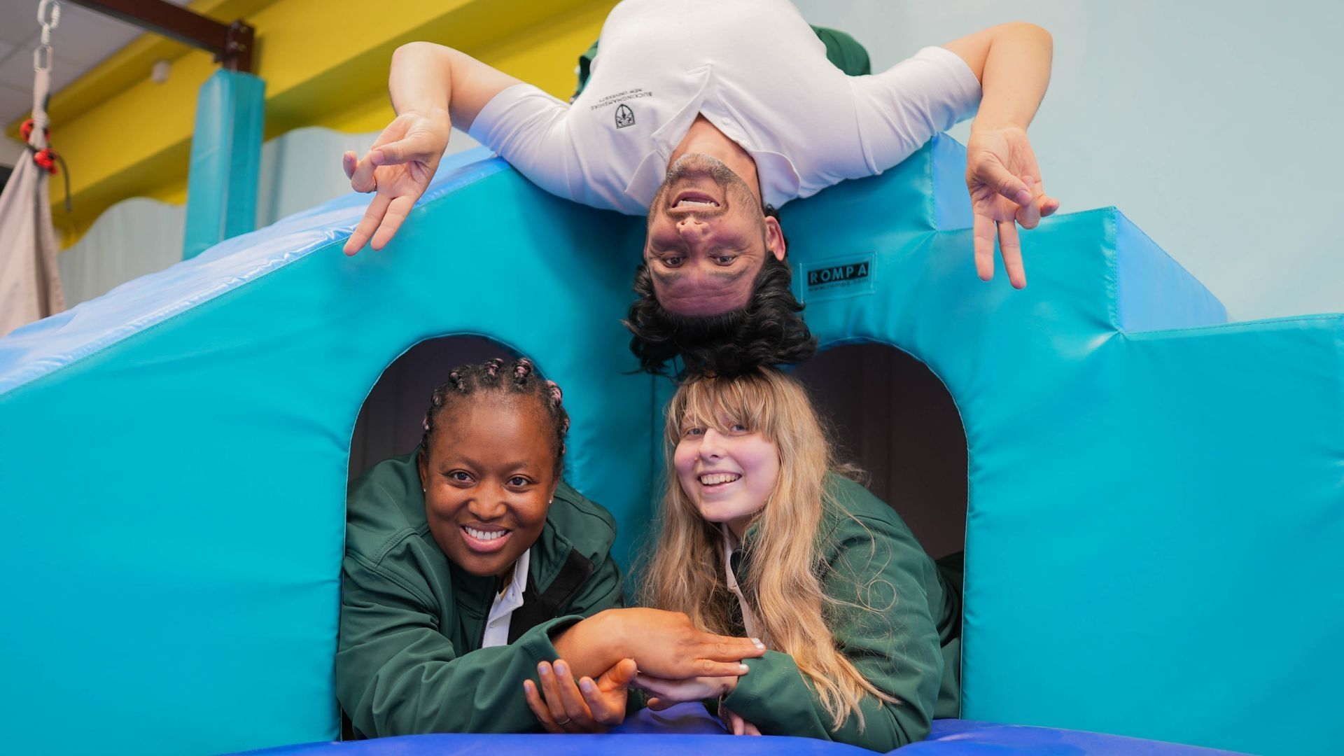 Two Occupational Therapy students laid down alongside one another as another student hands upside down.