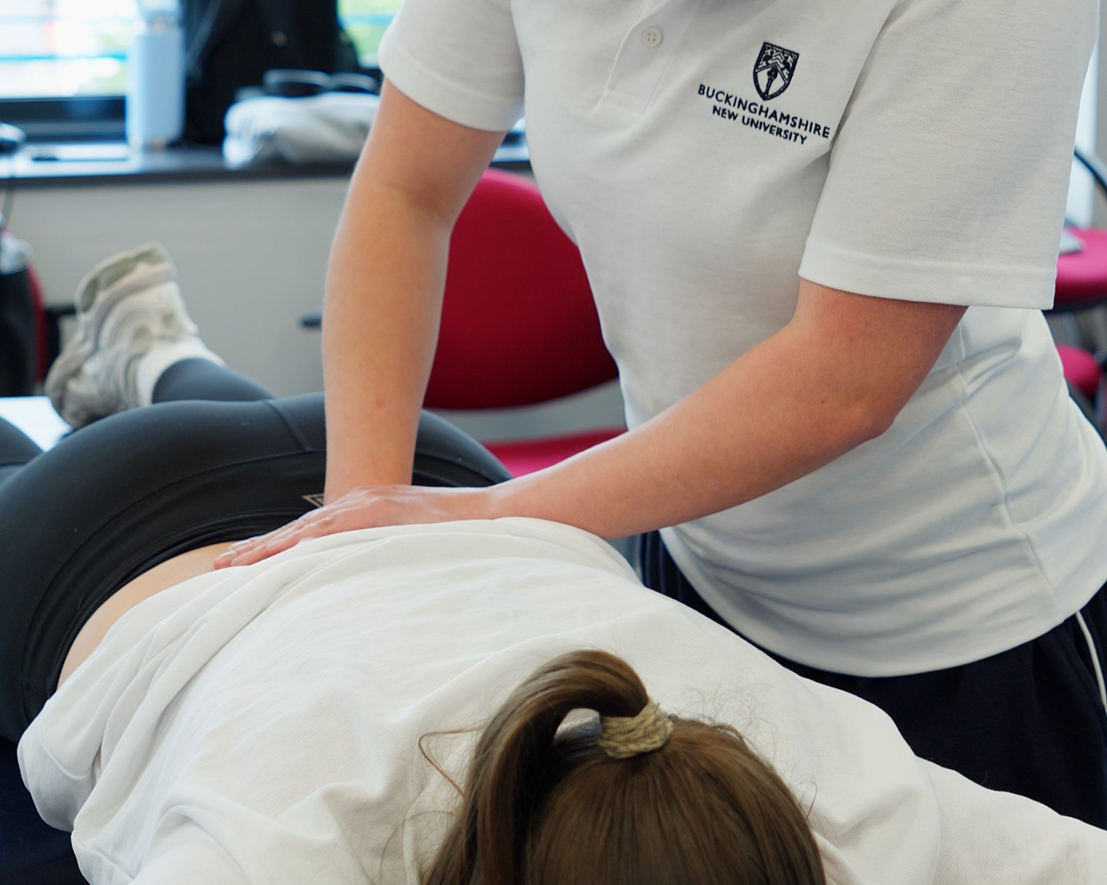 Physiotherapy student practicing lower back palpation and manual therapy techniques on a colleague lying face down on a treatment table