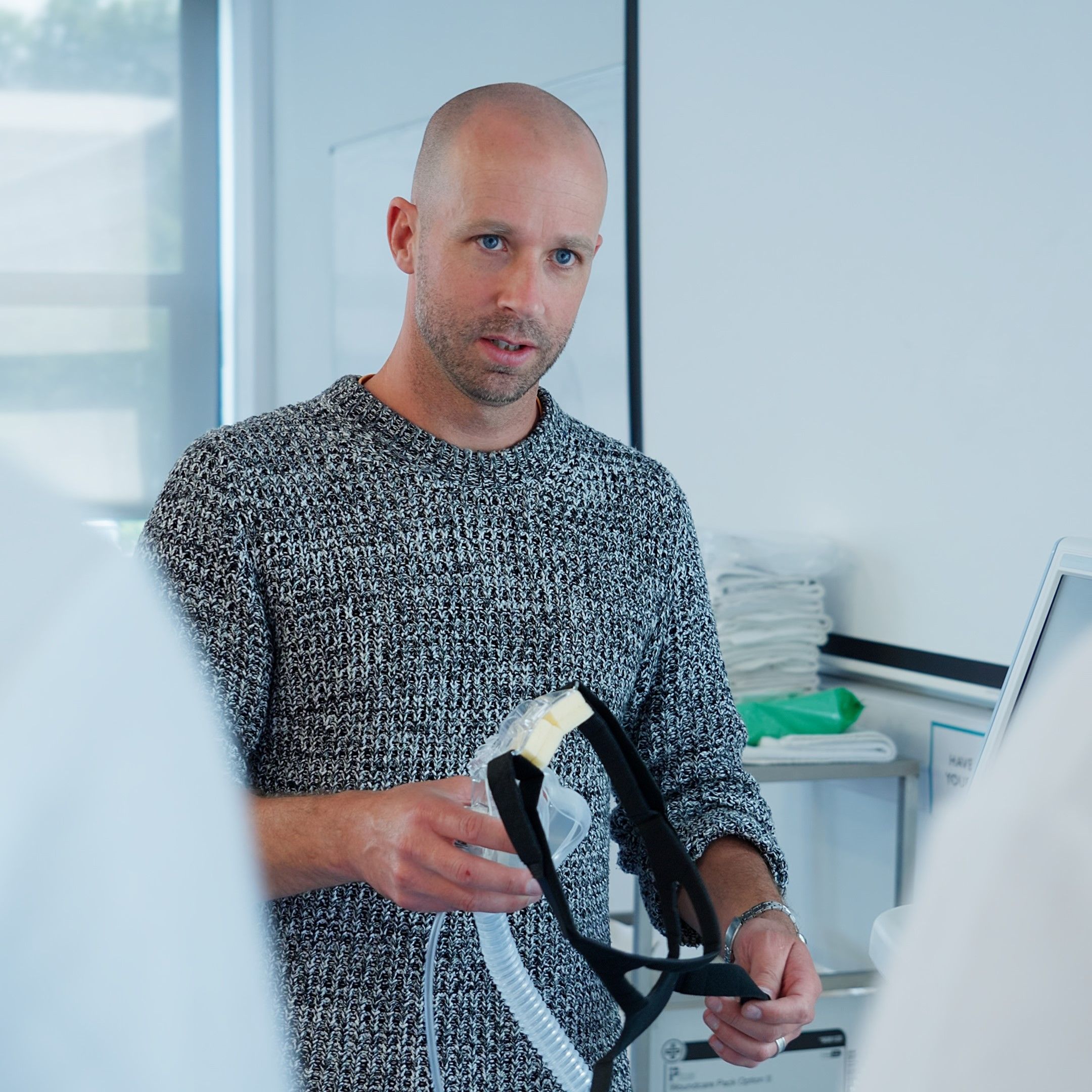 A Physiotherapy lecturer stood up in a classroom holding a piece of clinical apparatus in his right hand.