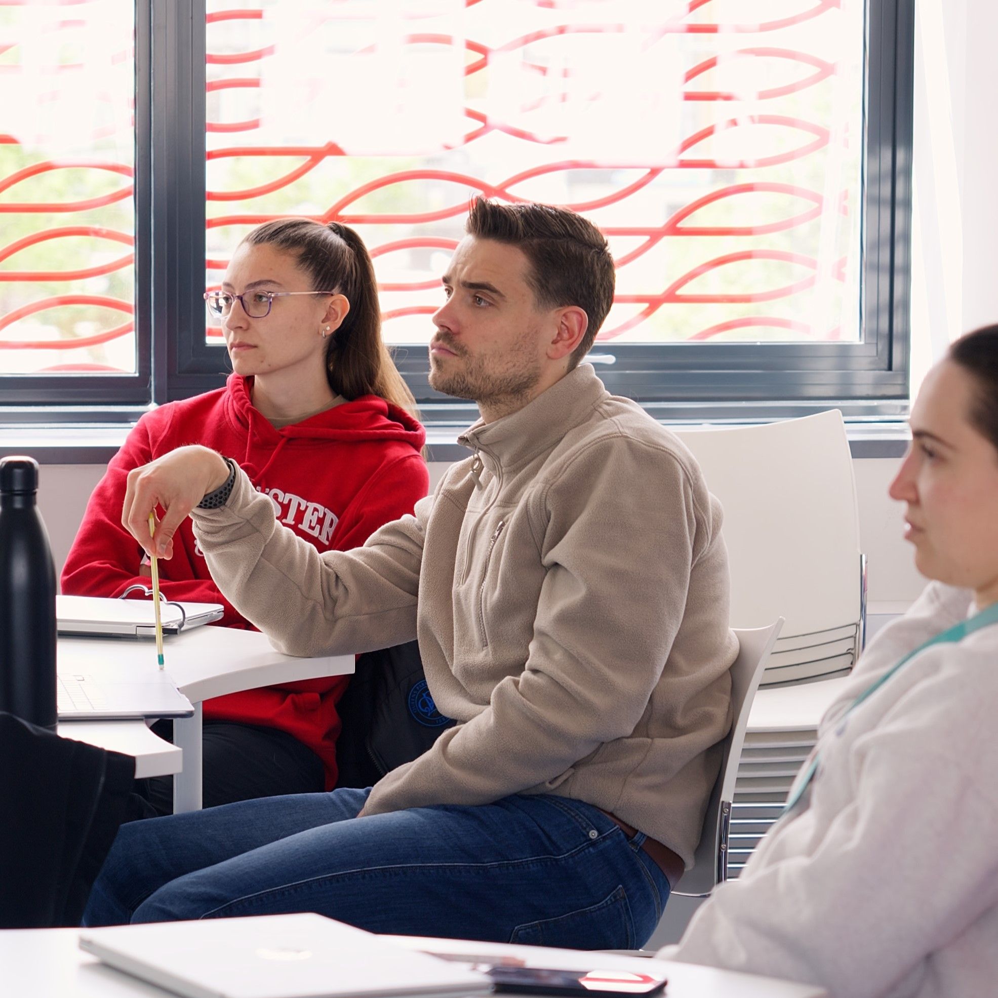 Three physiotherapy students sat around a table looking towards the front of a classroom